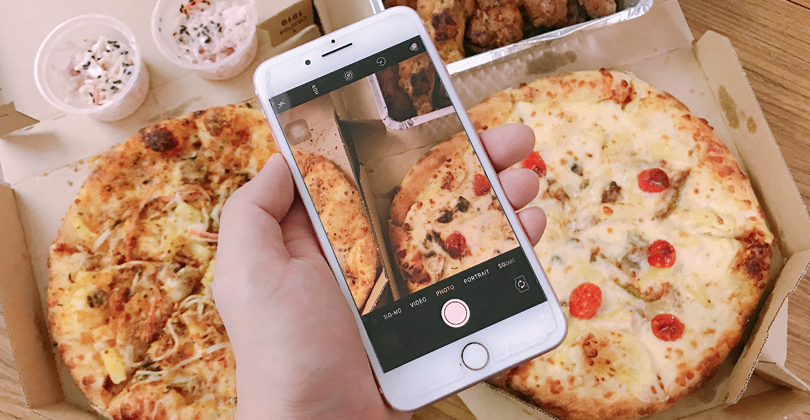 Mão de uma pessoa segurando um celular com a câmera ligada, apontando para as duas pizzas que ele pediu no delivery.
