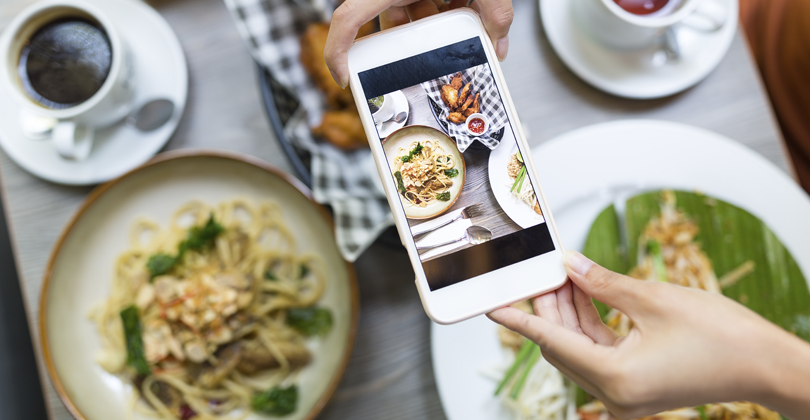 Mãos de uma mulher com um telefone fotografando as comidas para seu cardápio que vende